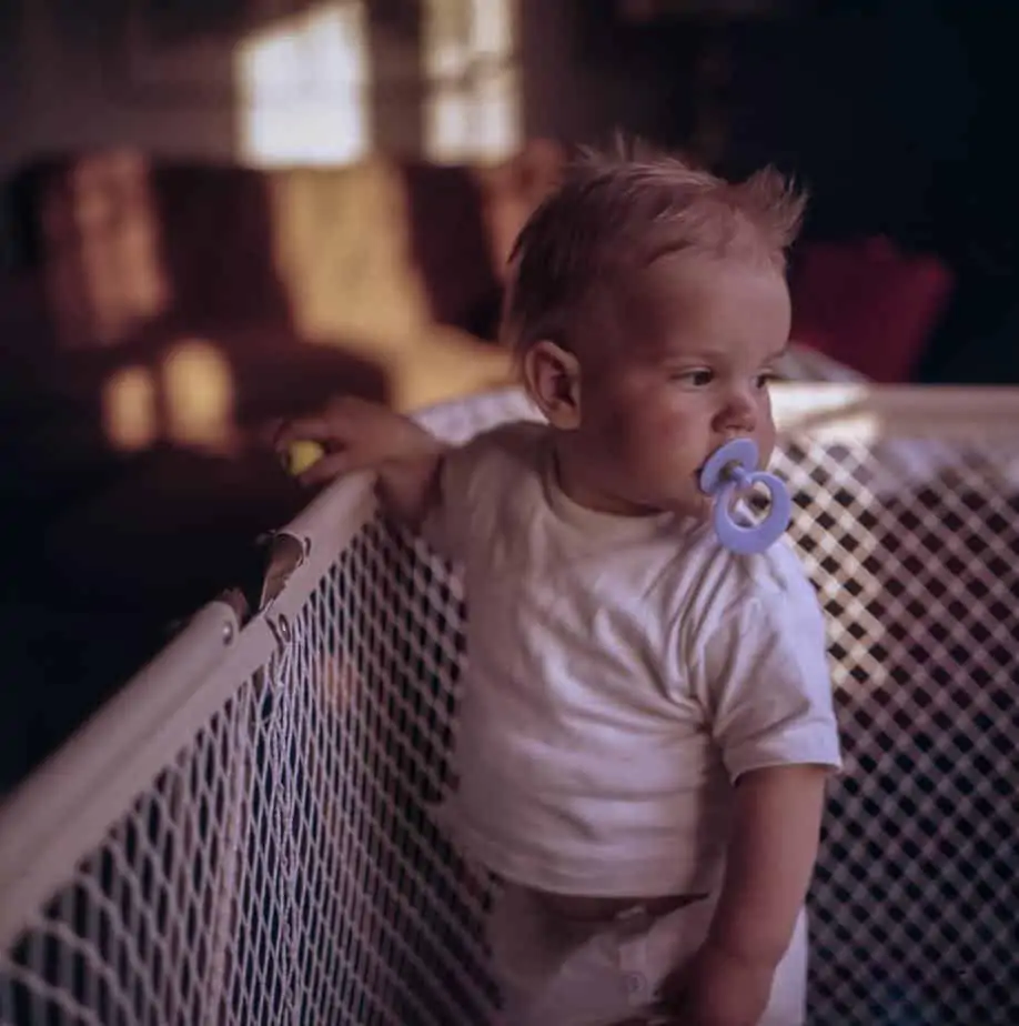 baby with pacifier in the mouth standing on crib